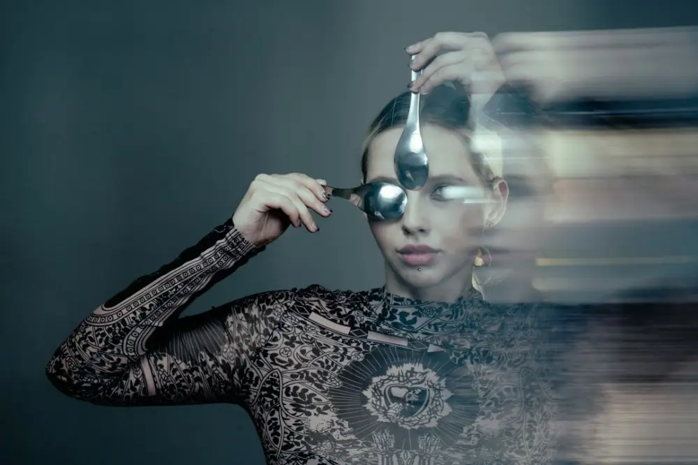 A person holding two silver spoons over their eyes in a double exposure portrait, illustrating everyday individuality